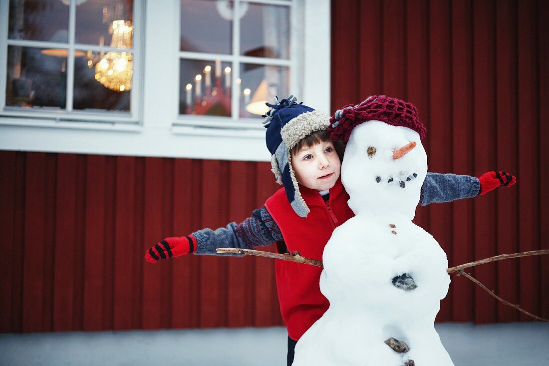 Kleiner Junge spielt mit Schneemann vor dem Haus