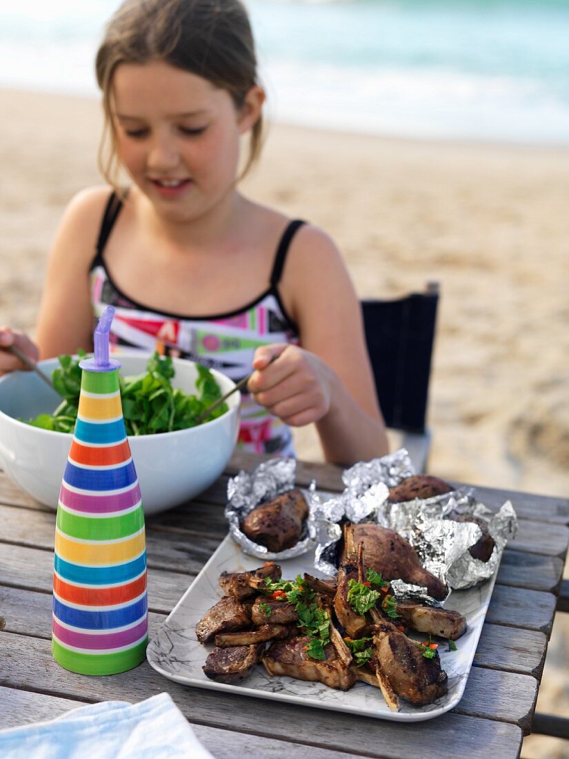 Mädchen beim Picknick am Strand mit Salat & Grillfleisch
