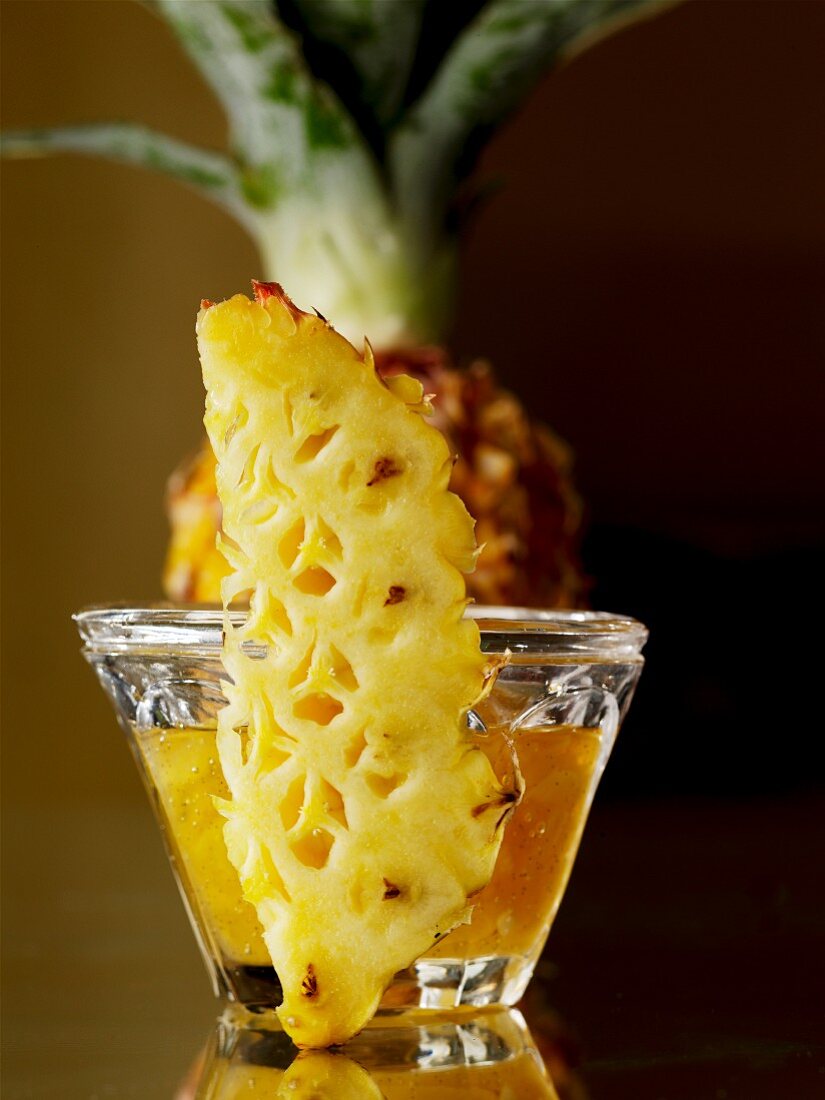 A wedge of pineapple in front of a glass of pineapple jam