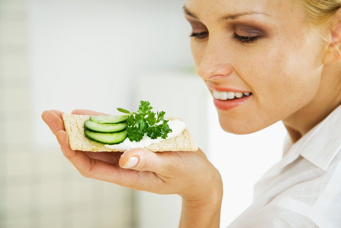 Woman holding up cracker with cucumber slices, smiling