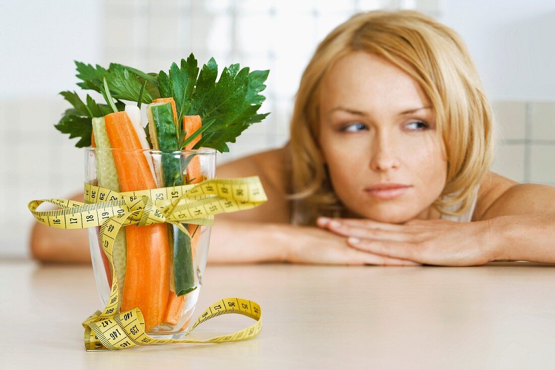 Woman contemplating glass filled with fresh vegetables wrapped with measuring tape tied in bow