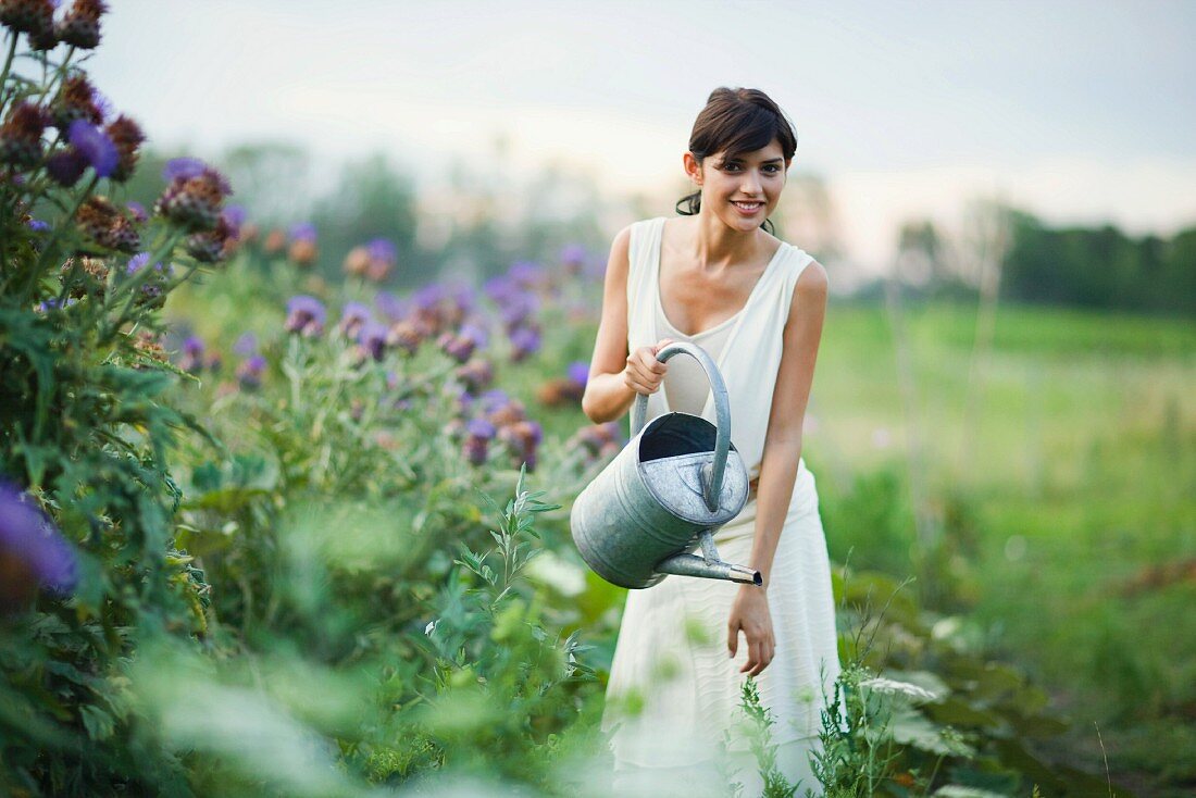 Young woman watering plants in garden with watering can, smiling at camera