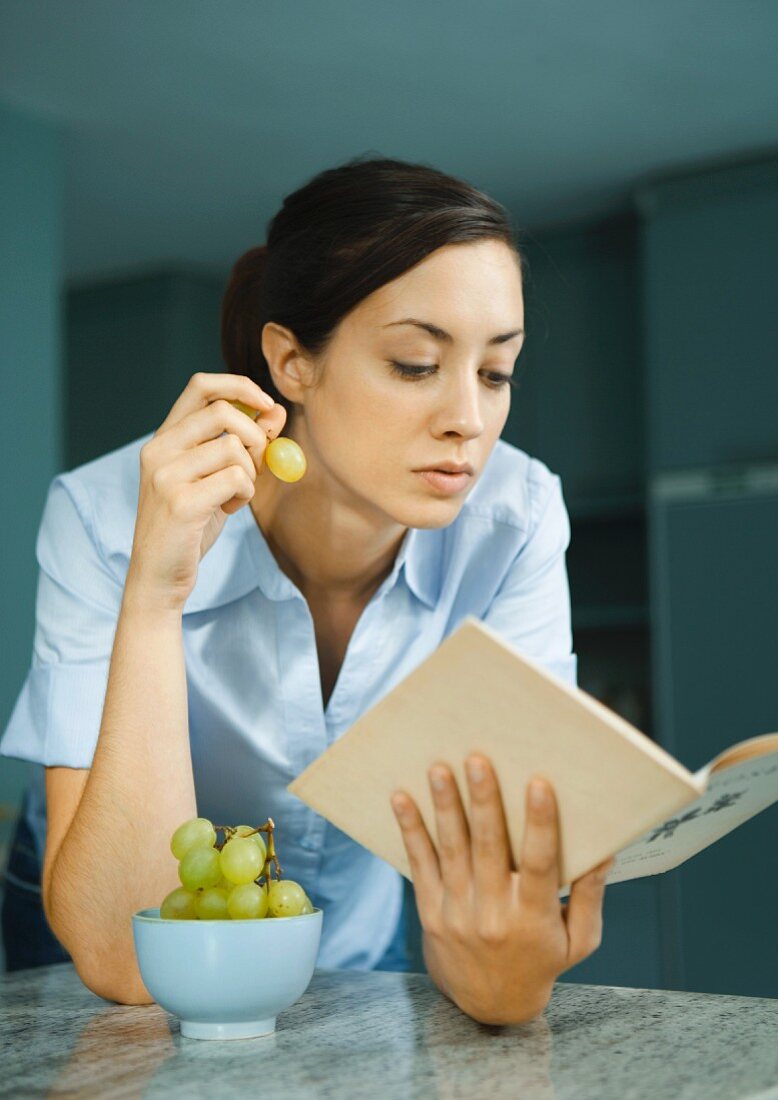 Woman reading book and eating grapes