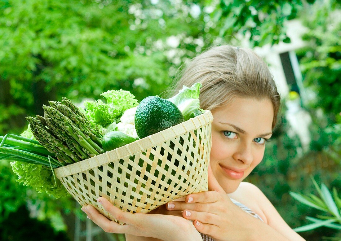 Junge Frau hält einen Korb mit grünem Gemüse