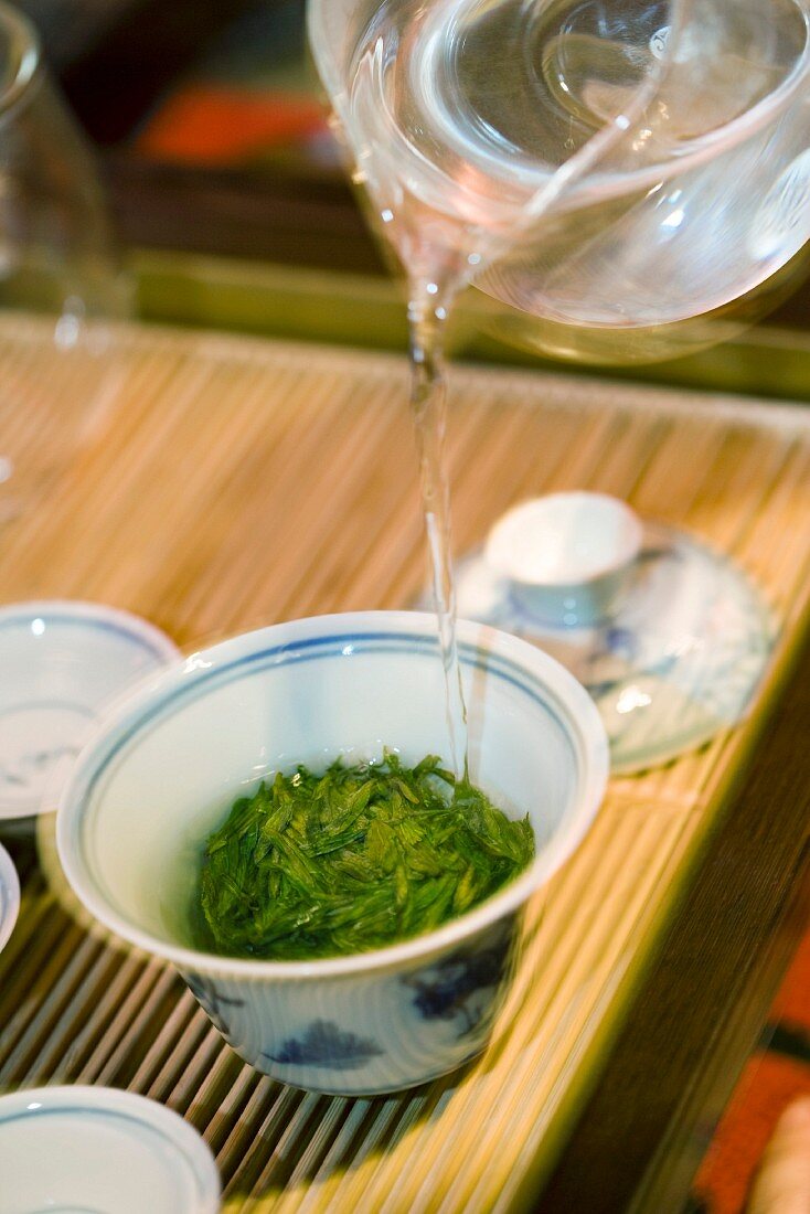 Hot water poured from glass teapot over tea leaves in gaiwan cup