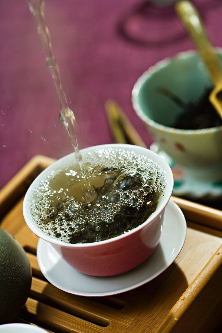 Hot water being poured and splashing over tea leaves in tea cup