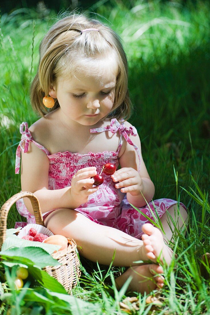 Kleines Mädchen sitzt mit Kirschen auf der Wiese
