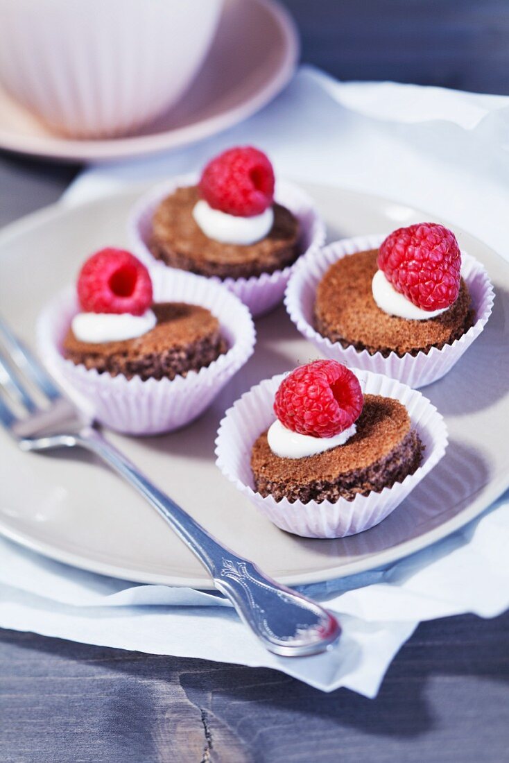 Round sponge cake topped with cream and raspberries on a plate
