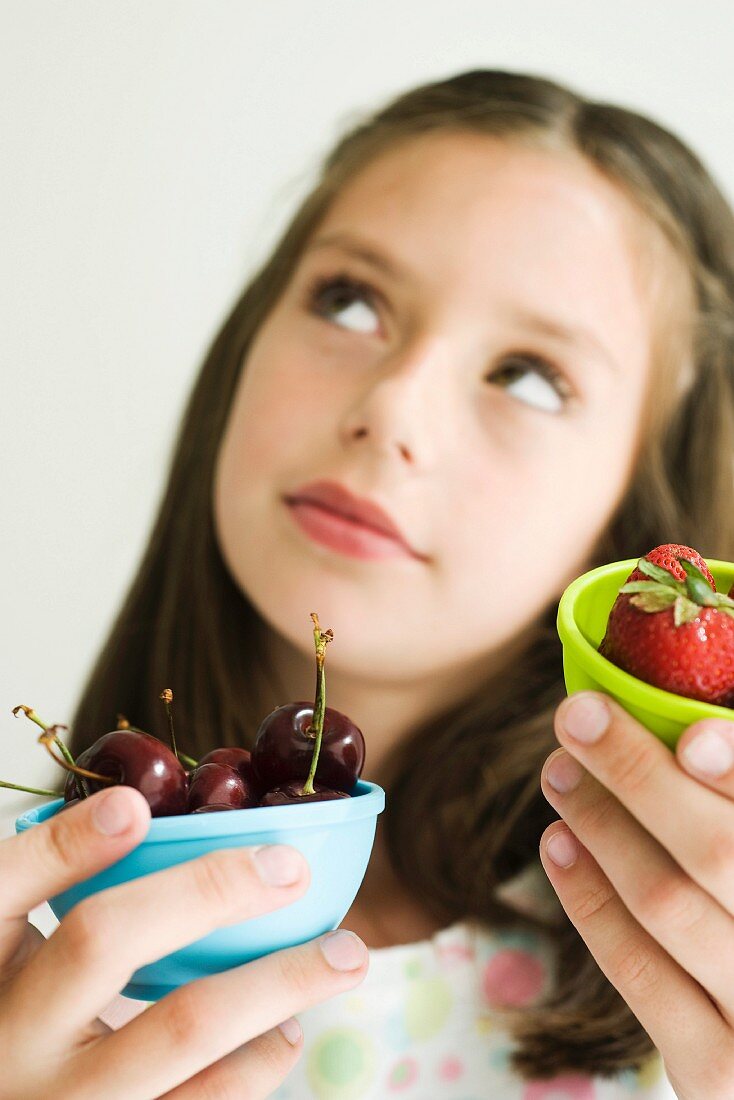 Girl deciding between bowl of cherries and bowl of strawberries