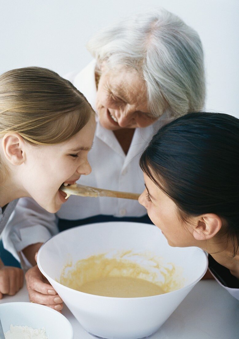 Grandmother baking with granddaughters, one girl tasting batter