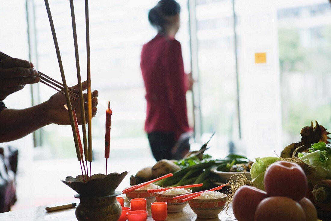 Food and candles on table as religious offering, person lighting incense