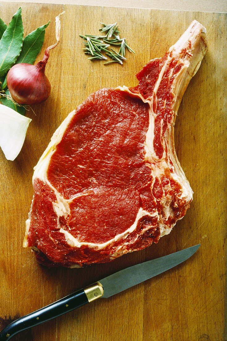 Raw steak on cutting board with herbs and knife, high angle view