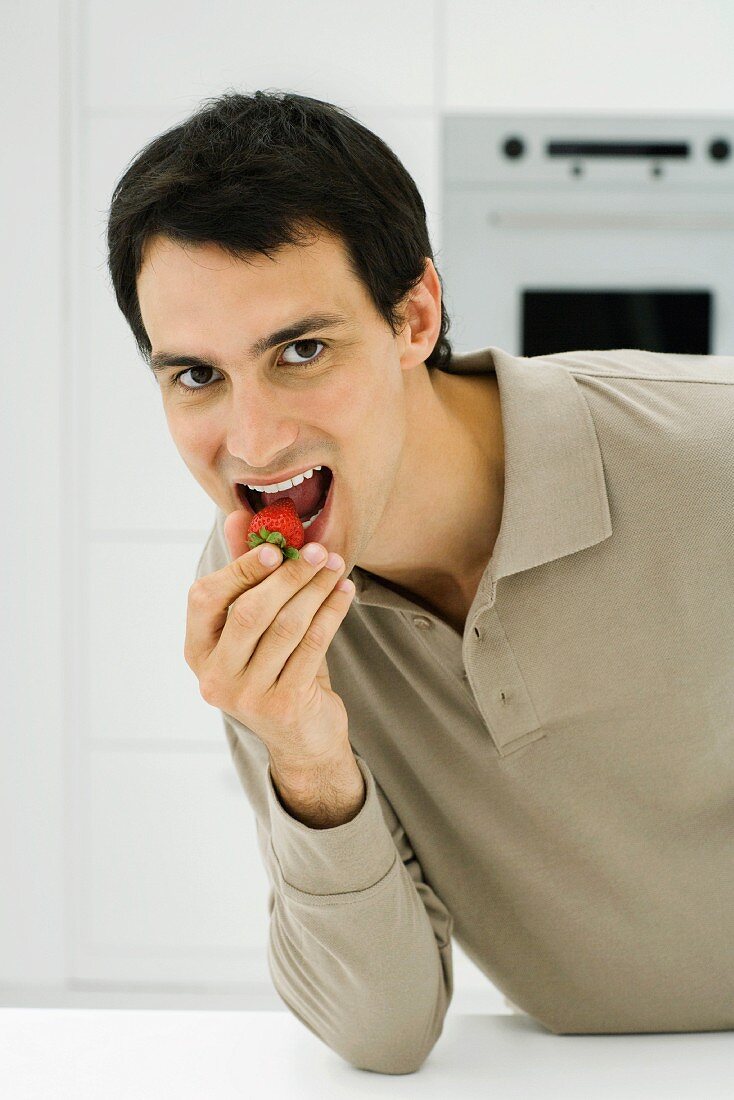 Man eating strawberry, looking at camera, close-up