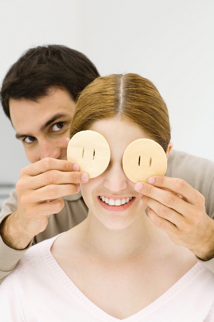 Young couple, man holding slices of fruit over woman's eyes
