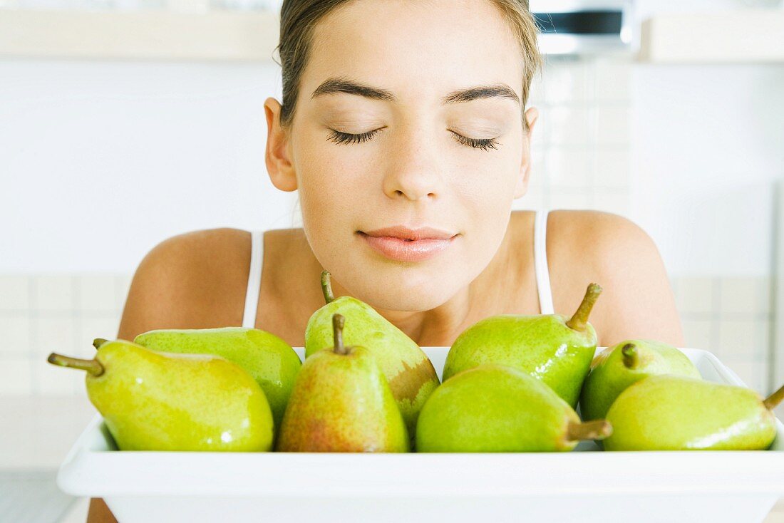 Young woman smelling fresh pears, eyes closed, close-up