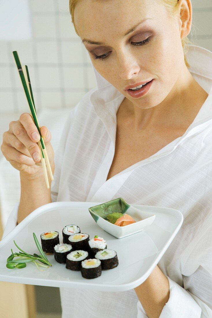 Frau hält einen Teller Maki-Sushi und Essstäbchen