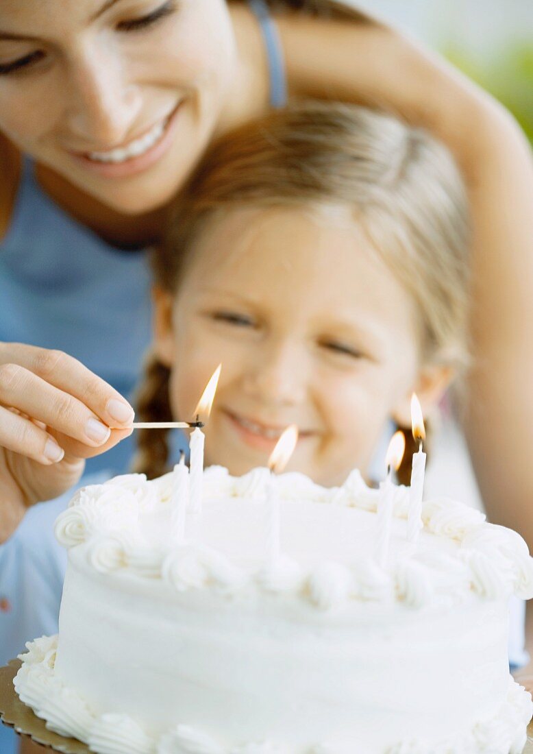 Mother lighting candles on birthday cake for daughter