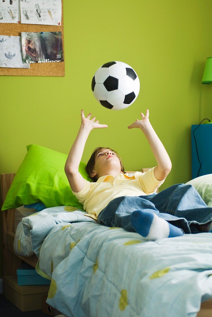 Kind liegt auf Bett und spielt mit dem Ball