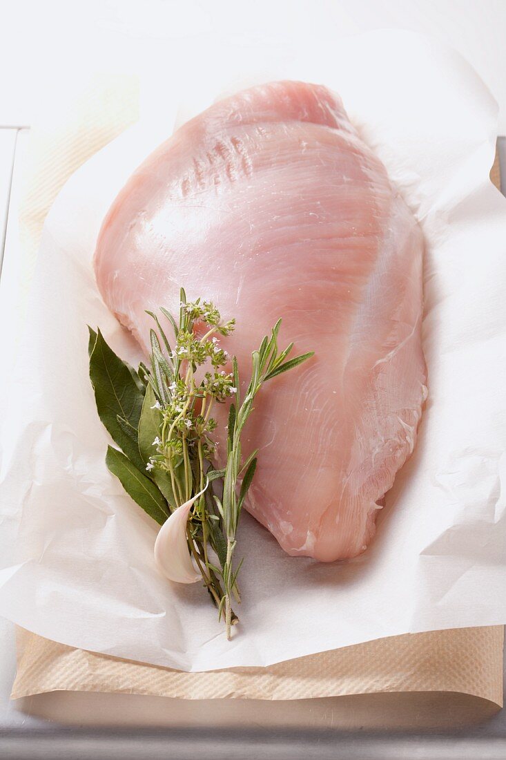 Turkey breast with herbs and garlic cloves on a piece of paper