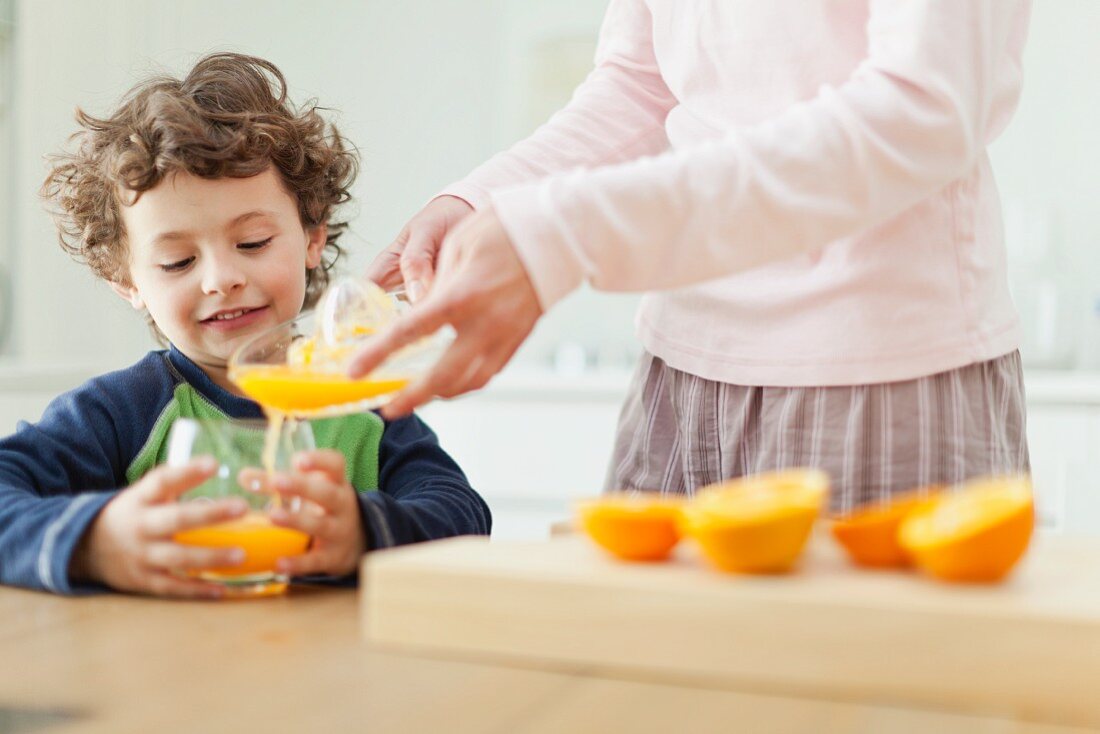 A mother pouring orange juice for a her son