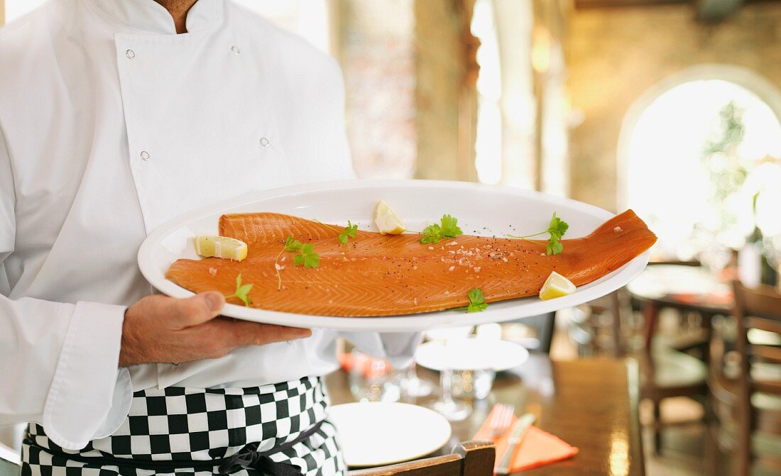 A cook holding a plate of smoked salmon