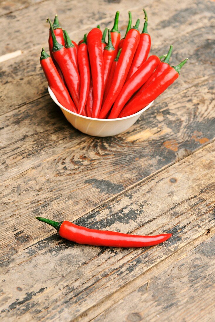 Chilischoten in einem Schälchen und auf dem Tisch