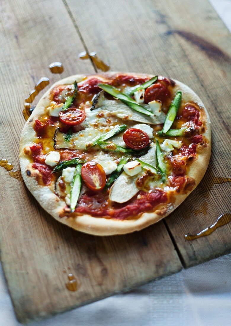 A pizza topped with king trumpet mushrooms, asparagus, goat's cheese and tomatoes