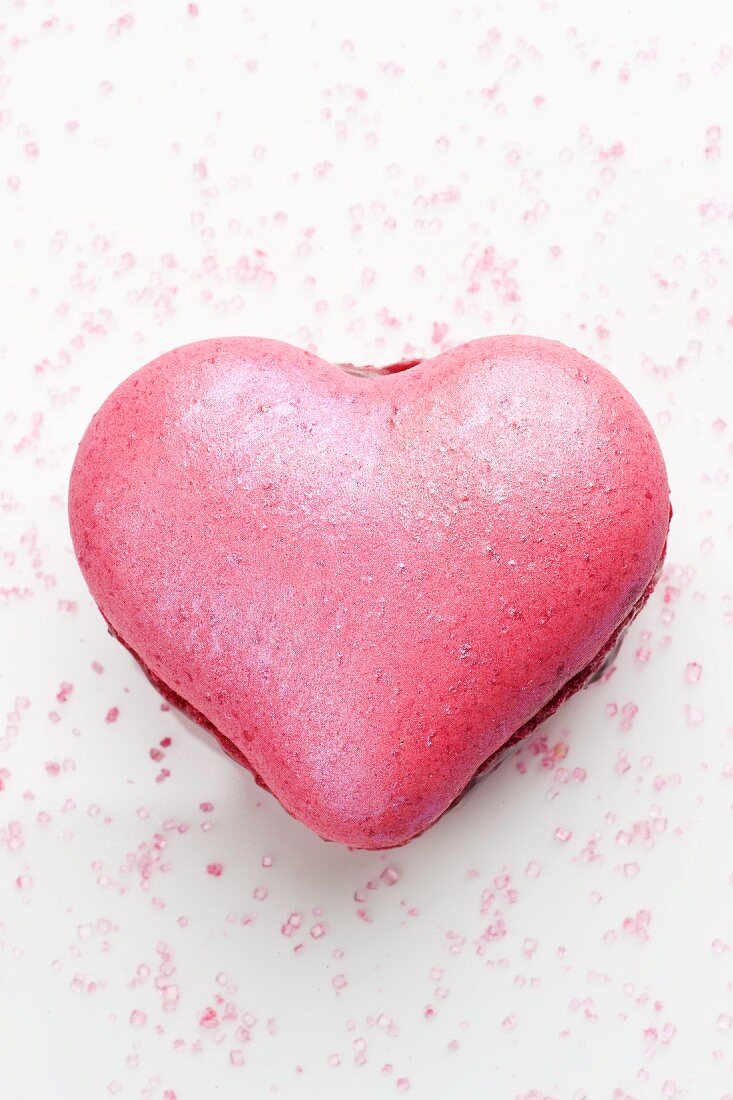 A pink, heart-shaped macaroon filled with jam