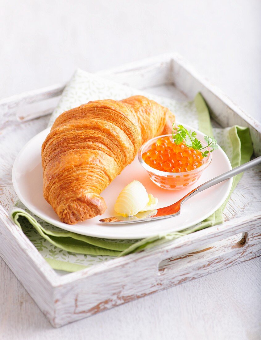 A croissant with caviar and butter on a wooden tray