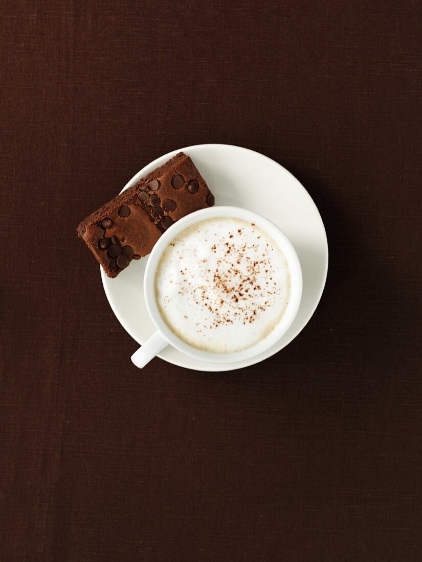 A cup of coffee with milk foam and a brownie (seen from above)