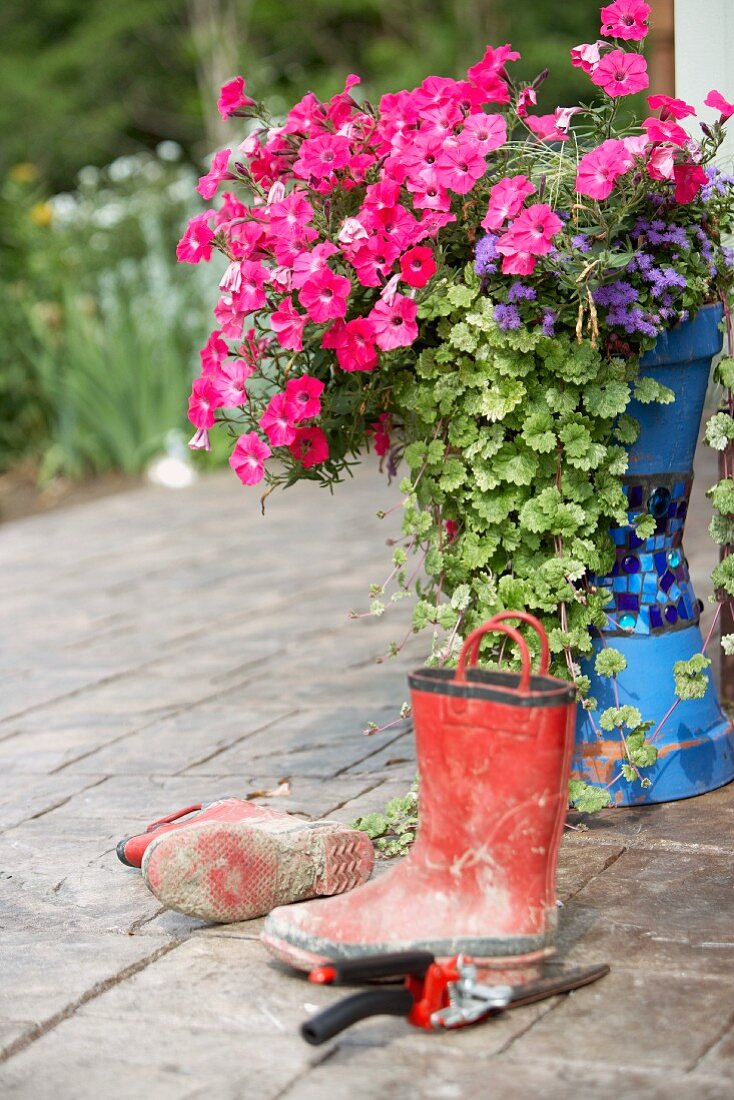 Gummistiefel und blühender Blumentopf auf Terrasse