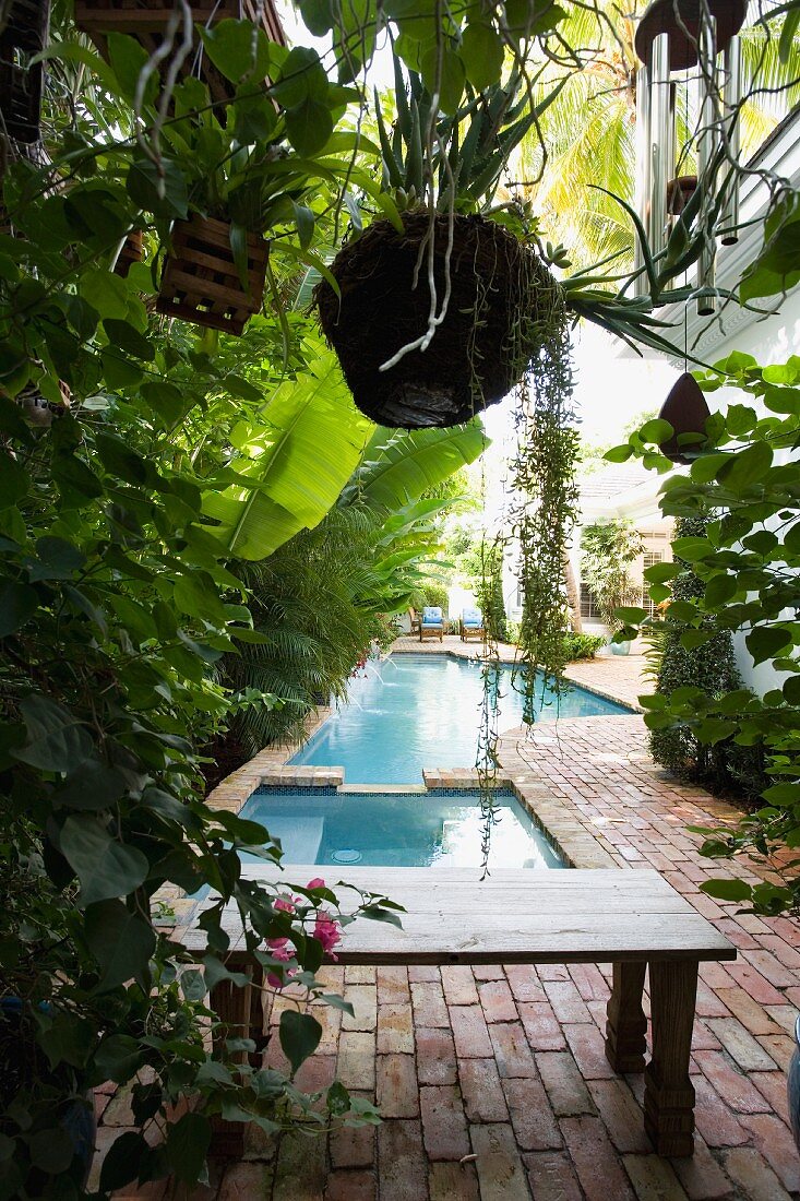 Tropisch-mediterraner Garten mit Ziegelpflaster und Poolanlage vor dem Haus