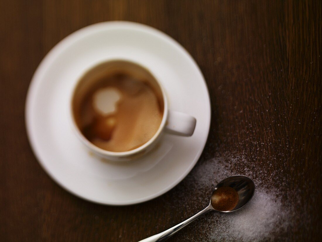 A cup of cappuccino with sugar sprinkled next to it