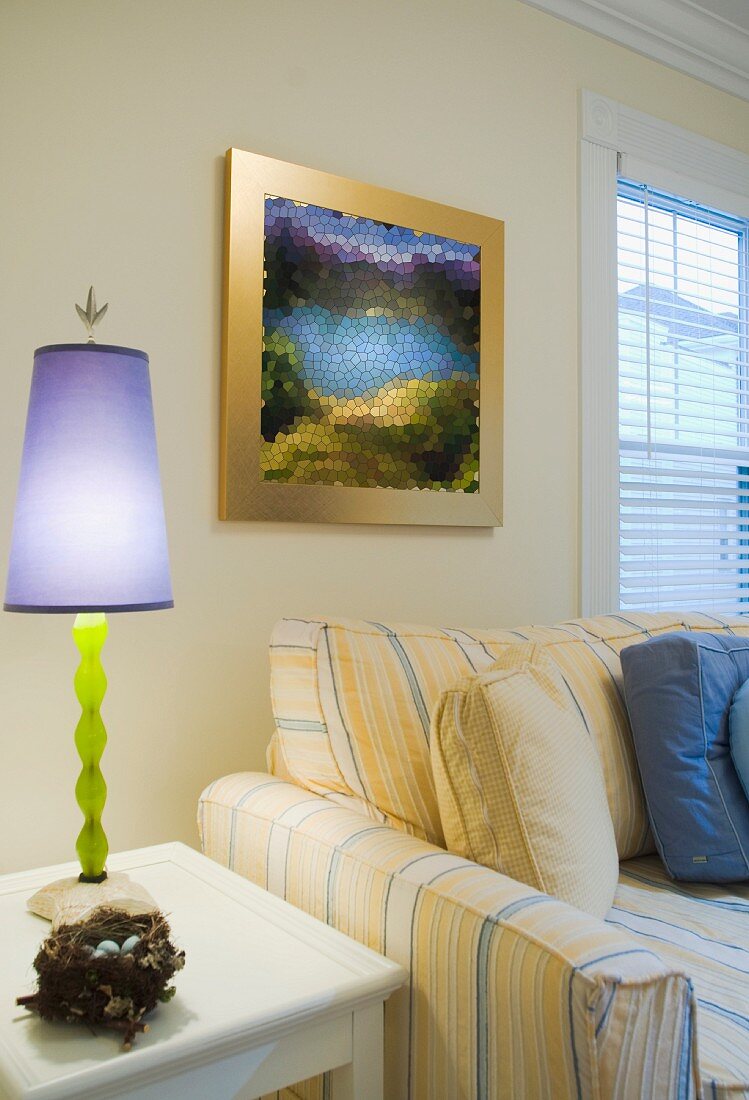 Purple lamp on end table near yellow and blue striped sofa