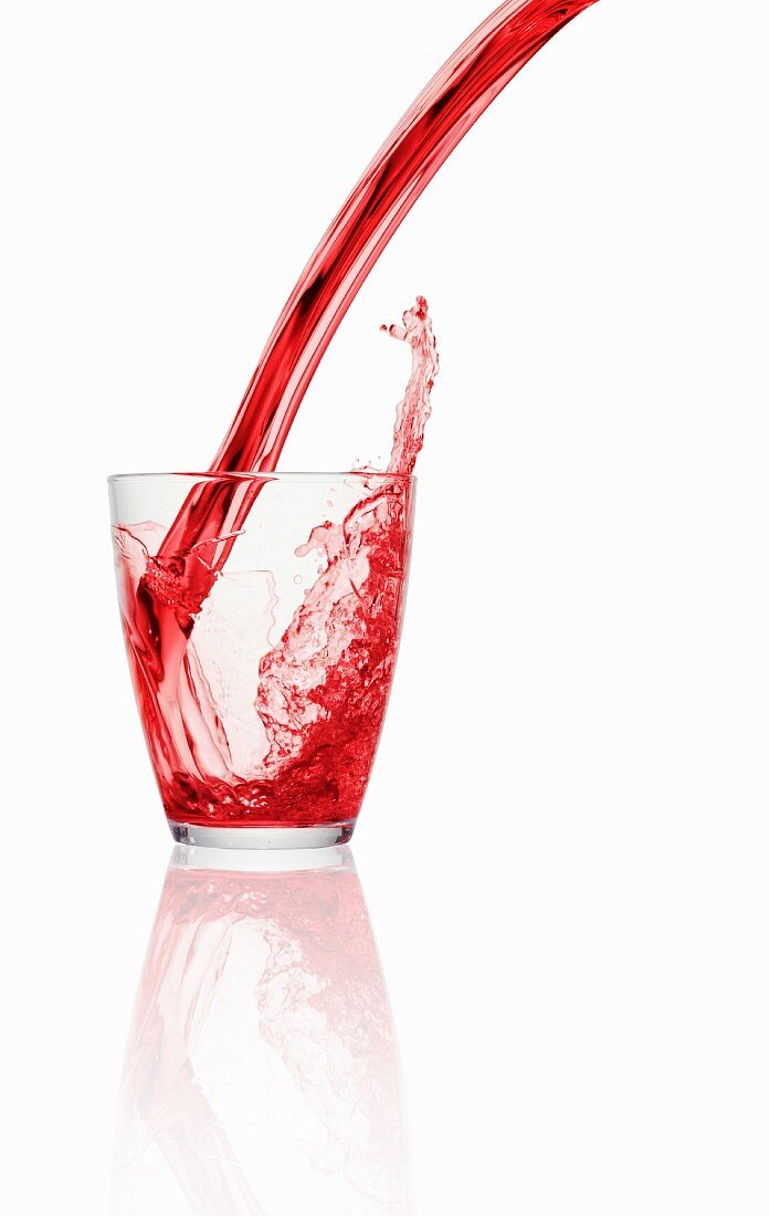 A red fizzy drink being poured into a glass