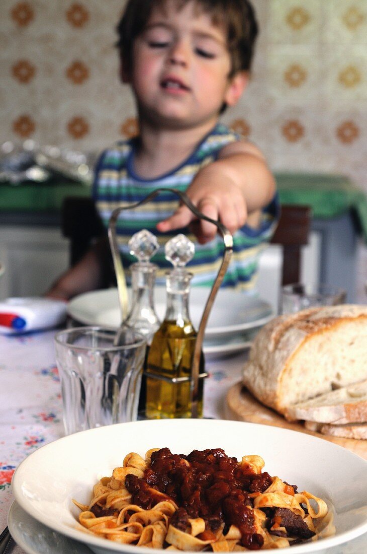 Kleiner Junge am Tisch sitzend zeigt auf Teller mit Tagliatelle
