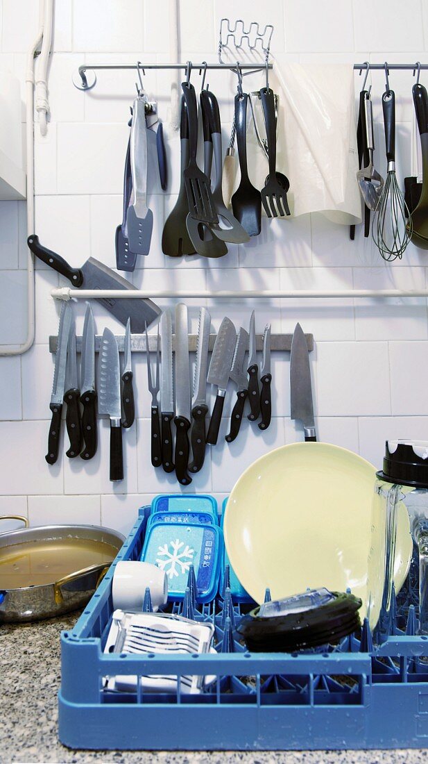 Various kitchen utensils hanging on the wall and a box of crockery in a commercial kitchen
