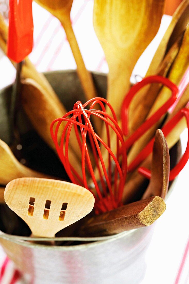 Wooden spoons, an egg whisk and other cooking utensils in a bucket