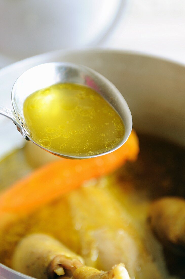 A ladle of chicken broth above a pot of soup