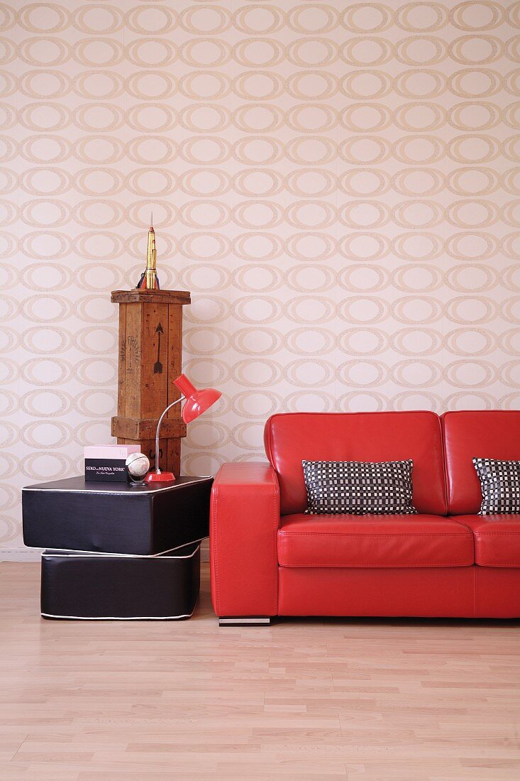 Partially visible glossy red leather couch next to table lamp on stacked floor cushions against op art wallpaper