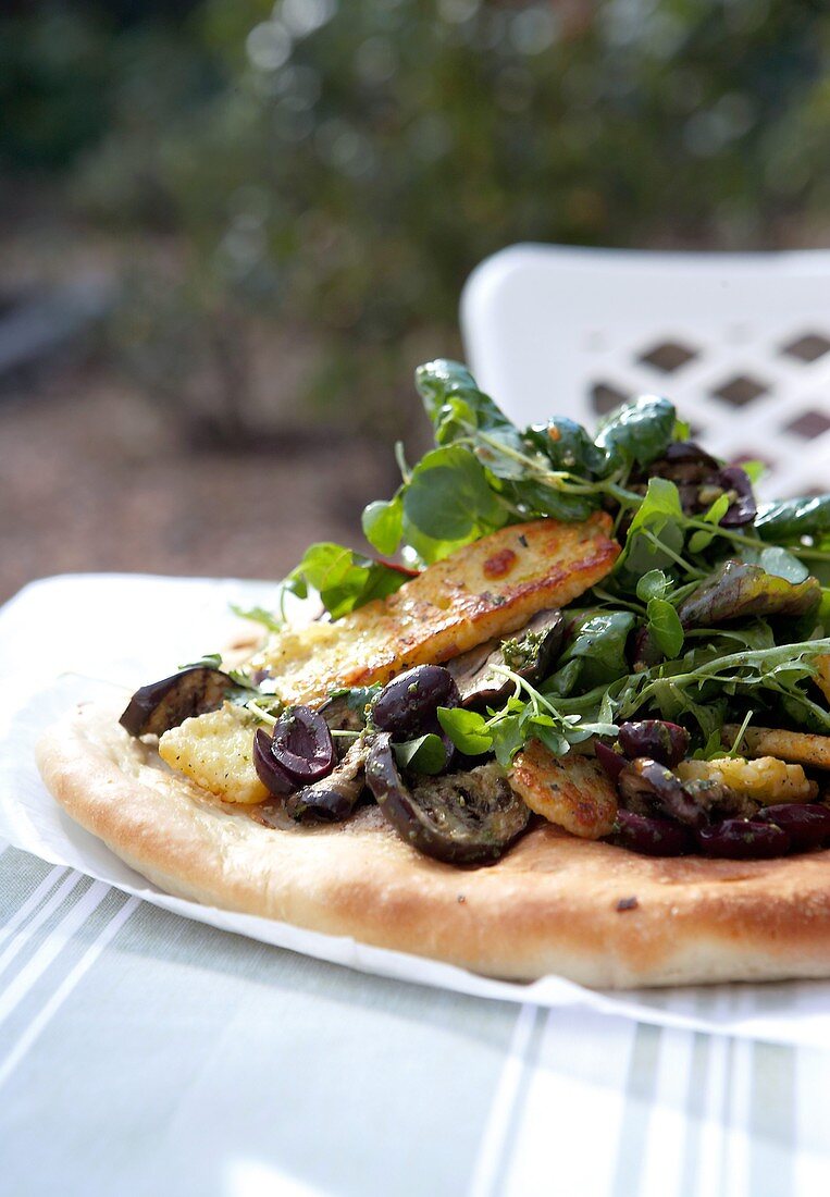 Unleavened bread topped with fried aubergines, Halloumi and herb salad