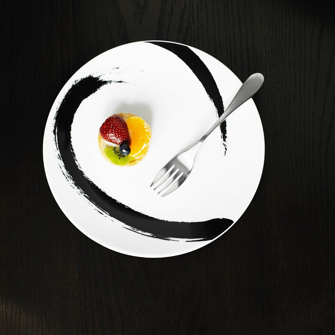 Mini Fruit Tart on a Black and White Plate; Fork