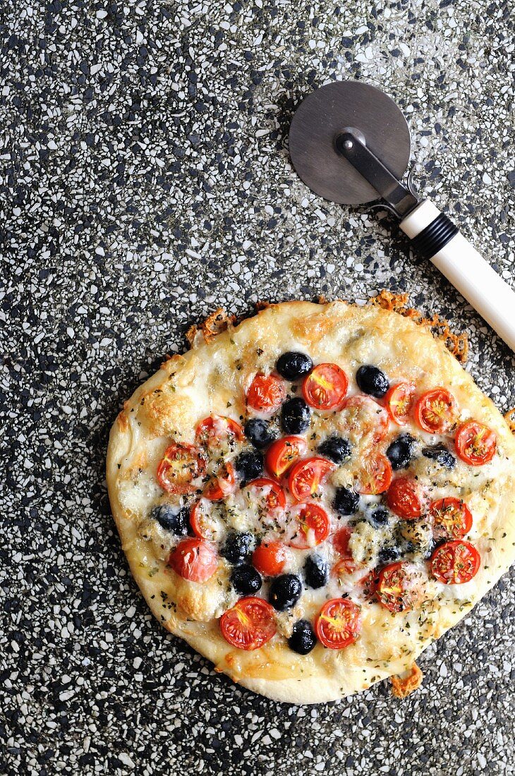 Pizza topped with gorgonzola and mozzarella cheese with cherry tomatoes and black olives