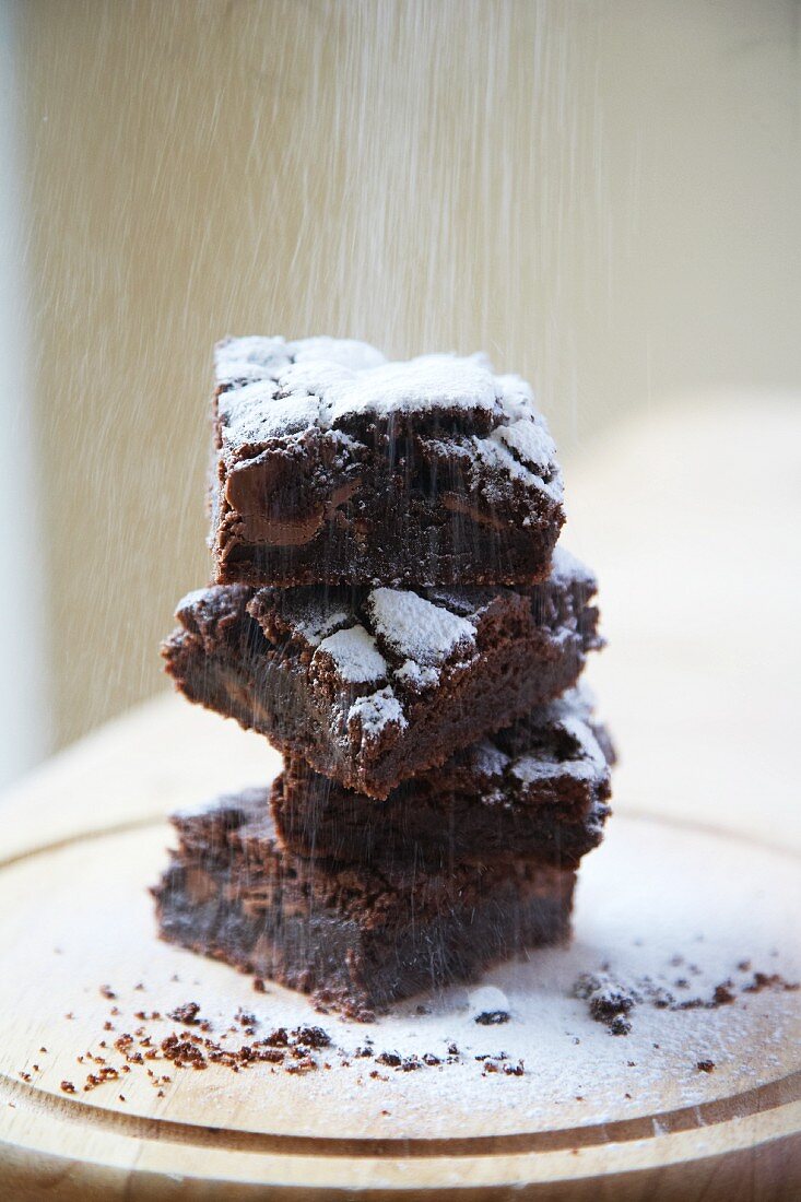 A stack of brownies being dusted with icing sugar
