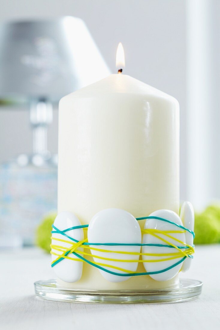 White pillar candle decorated with pebbles and rubber bands