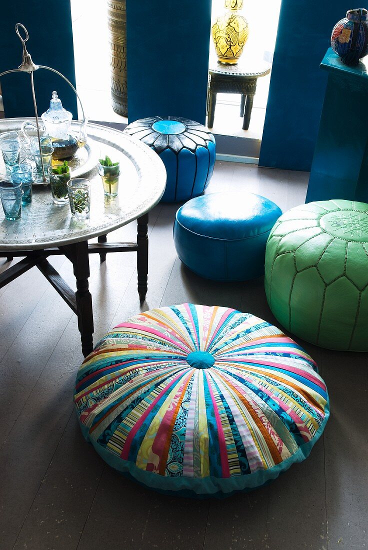 Pouffes with different covers next to side table holding Oriental-style metal tray