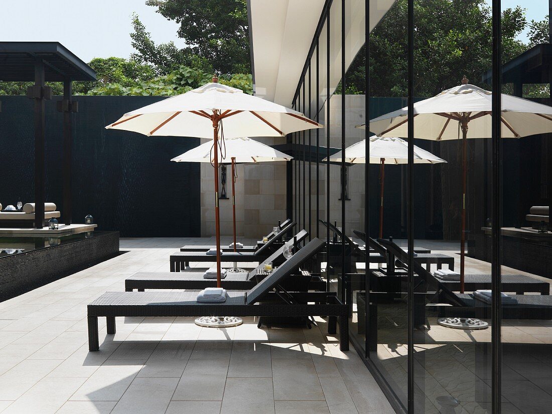 Contemporary outdoor furniture with parasol on tiled terrace against glass facade of apartment building