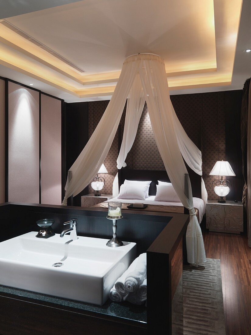 View across washstand to four-poster bed with canopy in classic, modern bedroom