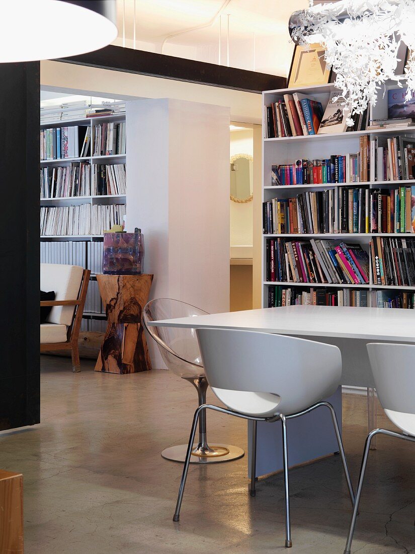 Retro shell chairs at table in front of bookcase in open-plan interior