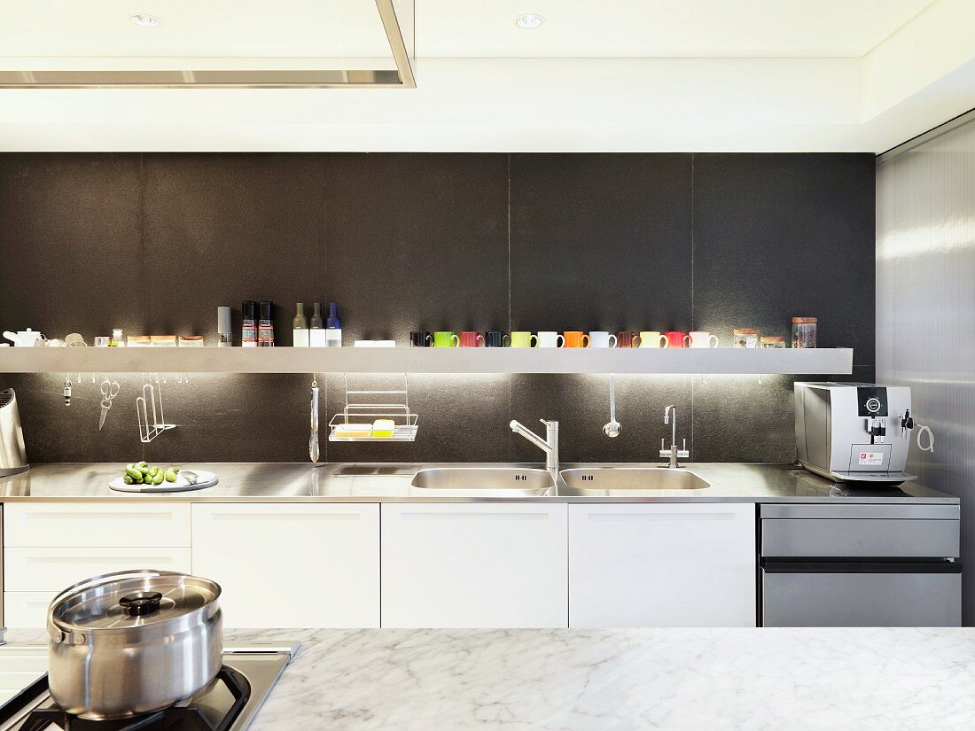 Designer kitchen with white kitchen units and backlit shelf against dark-grey wall